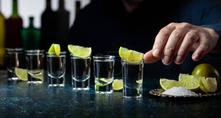Téléchargez les photos : Tequila avec tranches de sel et de citron vert sur une table bleu foncé. - en image libre de droit