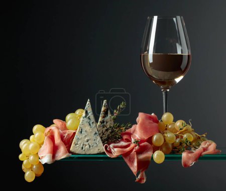 Foto de Copa de vino blanco con aperitivos. Uvas con queso azul, jamón y tomillo. Copiar espacio. - Imagen libre de derechos