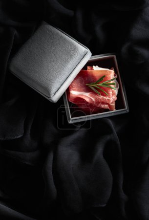 Téléchargez les photos : Prosciutto au romarin dans une boîte cadeau grise. Concept du thème de la nourriture chère. Vue du dessus. - en image libre de droit