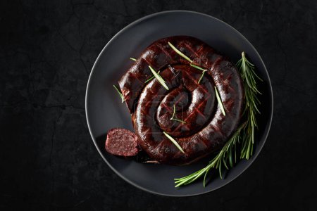 Photo for Black pudding or blood sausage with rosemary on a black plate. Top view. Copy space. - Royalty Free Image