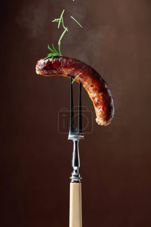 Téléchargez les photos : Saucisse bavaroise grillée au romarin. Saucisse sur une fourchette saupoudrée de romarin. Espace de copie. - en image libre de droit