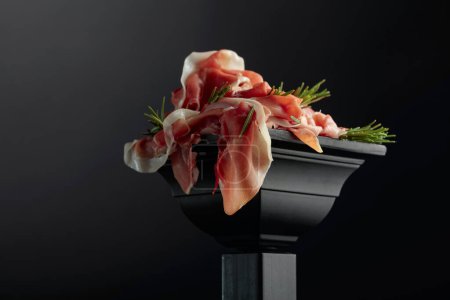 Photo for Prosciutto with rosemary on a black podium. Copy space. - Royalty Free Image