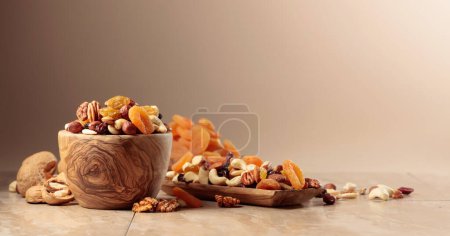 Téléchargez les photos : Fruits secs et noix sur une table en céramique beige. Mélanger les noix, les abricots et les raisins secs dans un bol en bois. Espace de copie. - en image libre de droit