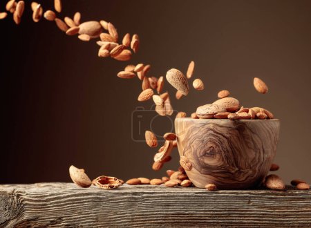 Photo for Almond is poured into a wooden bowl. Brown background with copy space. - Royalty Free Image