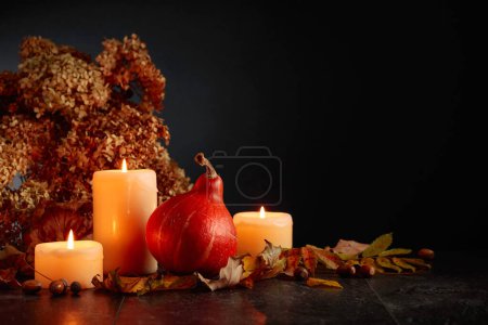 Photo for Still life with pumpkin, dried-up leaves, burning candles, and dried hydrangea flowers. Black background with copy space. Autumn concept. - Royalty Free Image