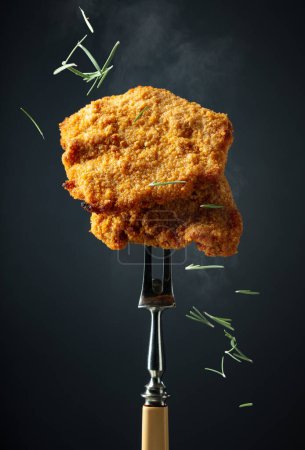 Foto de Schnitzel frito en un tenedor. Schnitzel panificado sobre fondo negro. - Imagen libre de derechos