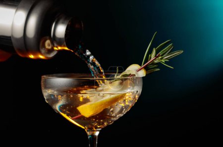 Foto de Gin tonic con romero y limón. El cóctel se vierte de una coctelera en un vaso. - Imagen libre de derechos