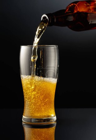 Photo for Pouring beer from a bottle into a glass. Glass of beer on a black reflective background. - Royalty Free Image