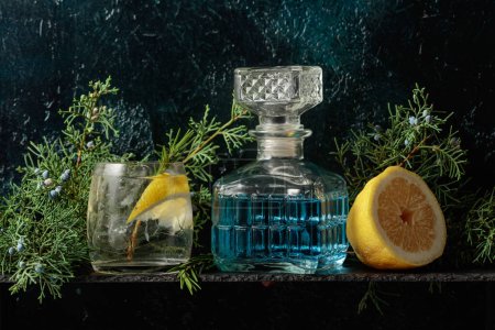 Foto de Cóctel gin-tonic con hielo, limón y romero en un vaso congelado. Una bebida refrescante con ramas de enebro sobre un fondo vintage azul oscuro. - Imagen libre de derechos