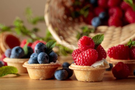 Téléchargez les photos : Petites tartelettes aux framboises et bleuets frais garnies de menthe sur une table en bois. - en image libre de droit