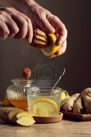 Foto de Té de jengibre con limón y miel en una mesa de cerámica marrón. El jugo se exprime de un limón con un exprimidor de madera viejo. - Imagen libre de derechos