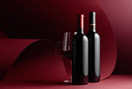 Téléchargez les photos : Bouteilles et verre de vin rouge sur fond rouge. Espace de copie. - en image libre de droit