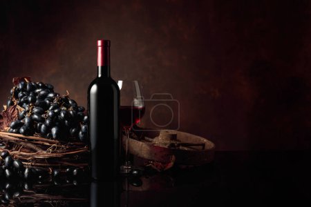 Téléchargez les photos : Verre et bouteille de vin rouge avec des raisins bleus sur fond noir réfléchissant. Espace de copie. - en image libre de droit