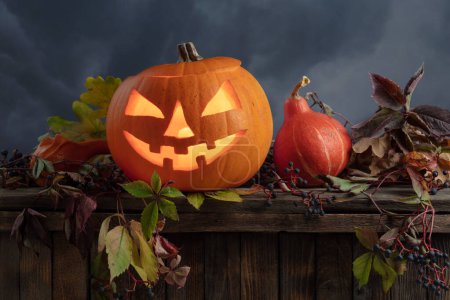 Photo for Halloween pumpkin head jack lantern with dried-up leaves. Halloween holidays art design. Carved Halloween pumpkin with burning candle on a background of cloudy sky. - Royalty Free Image