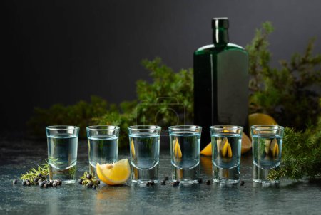 Téléchargez les photos : Du gin bleu et des branches de genièvre sur une vieille table bleu foncé. Gin aux baies de genièvre, tranches de citron et bouteille vintage. - en image libre de droit