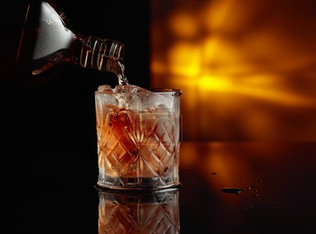 Photo for Pouring whiskey from a bottle into a glass with ice. Copy space. - Royalty Free Image