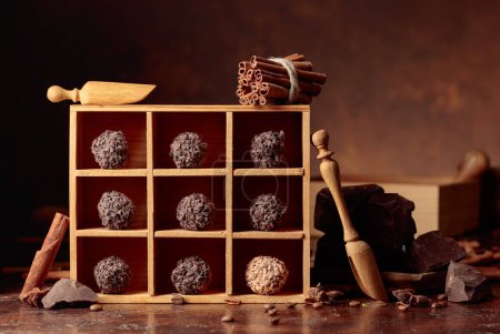 Photo for Chocolates in a wooden box. Broken pieces of chocolate, cinnamon sticks, anise and coffee beans on a brown background. - Royalty Free Image