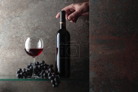 Téléchargez les photos : Main tendue pour une bouteille de vin rouge. Une image conceptuelle sur le thème des vins chers. Espace libre pour votre texte. - en image libre de droit