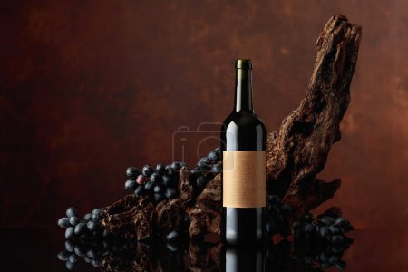 Foto de Botella de vino tinto con la vieja etiqueta vacía. En el fondo viejo enganche envejecido y uvas azules. Copiar espacio. - Imagen libre de derechos