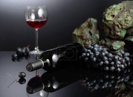 Téléchargez les photos : Raisins bleus et vin rouge sur fond noir réfléchissant. Espace de copie. - en image libre de droit