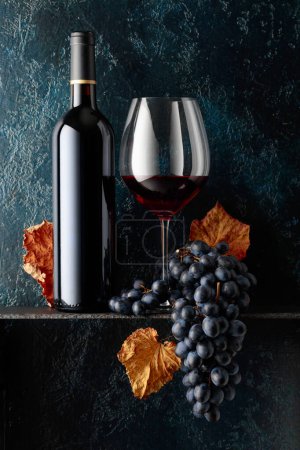 Foto de Vino tinto y uvas azules con hojas de vid secas sobre un viejo fondo azul oscuro. Copiar espacio. - Imagen libre de derechos