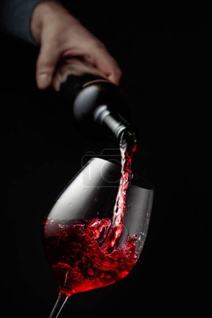 Photo for Pouring red wine in a glass goblet. Black background with copy space. - Royalty Free Image