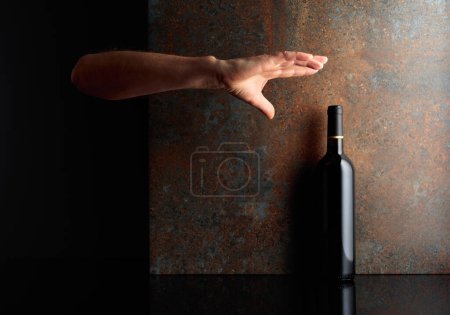 Téléchargez les photos : Main tendue pour une bouteille de vin rouge. Une image conceptuelle sur le thème des vins chers. Espace de copie. - en image libre de droit