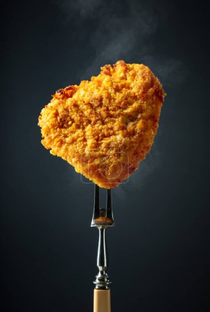 Téléchargez les photos : Schnitzel frit chaud sur une fourchette. Schnitzel pané sur fond noir. - en image libre de droit