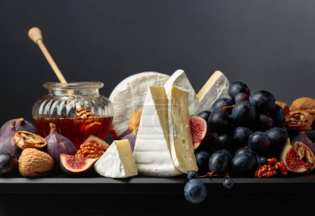 Foto de Queso Camembert con higos, uvas, nueces y miel. Queso suave con frutas sobre fondo negro. - Imagen libre de derechos