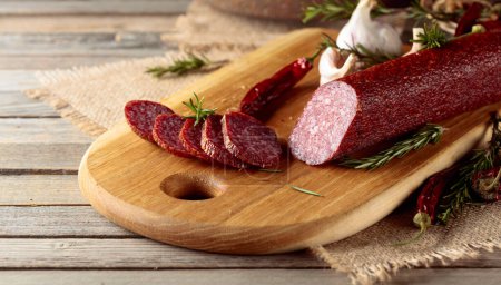 Photo for Salami on a cutting board. Sliced sausage with rosemary, red pepper, and garlic on an old wooden table. - Royalty Free Image