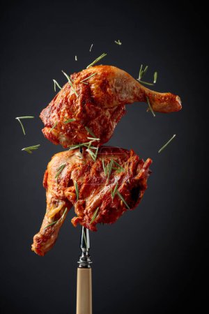 Téléchargez les photos : Jambes de poulet grillées chaudes saupoudrées de romarin sur un fond noir. Tambour de poulet sur une fourchette. - en image libre de droit