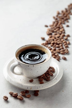 Téléchargez les photos : Café noir et grains de café sur une table blanche. Une goutte de café tombe dans une tasse. Espace de copie. - en image libre de droit