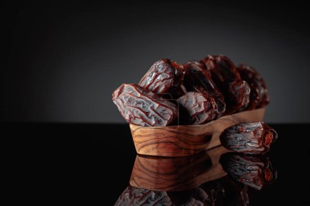 Photo for Raw ripe dates fruits on a wooden dish on a black background. Copy space. - Royalty Free Image
