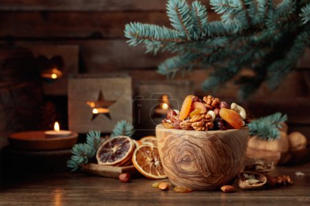 Téléchargez les photos : Fruits secs et noix assorties sur une vieille table en bois. Nature morte de Noël avec des branches d'épinette et des bougies allumées dans de vieilles lanternes. - en image libre de droit