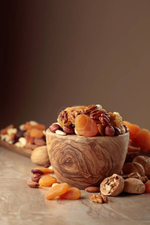 Foto de Frutas secas y frutos secos sobre una mesa de cerámica beige. La mezcla de nueces, albaricoques y pasas en un tazón de madera. - Imagen libre de derechos