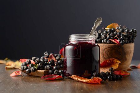 Photo for Chokeberry jam and fresh berries with leaves on an old wooden table. - Royalty Free Image