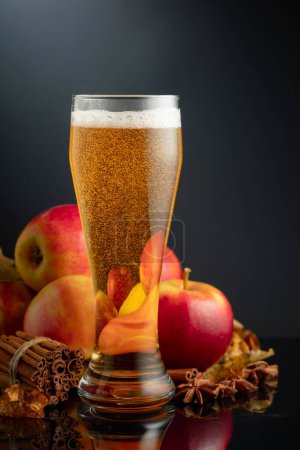Téléchargez les photos : Cidre de pomme en verre haut. Boisson fraîche aux pommes, cannelle et anis sur fond noir. - en image libre de droit