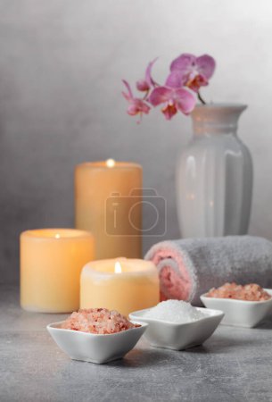 Téléchargez les photos : Sel marin, serviettes, fleurs d'orchidées et bougies allumées sur fond gris. Concept de spa avec espace de copie. - en image libre de droit
