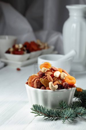 Photo for Dried fruits and assorted nuts on a white wooden table with a green spruce branch. - Royalty Free Image