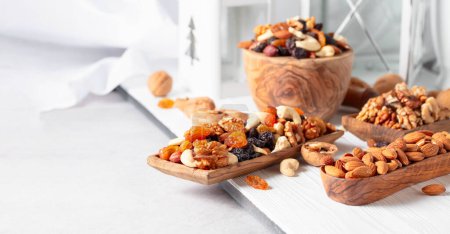 Téléchargez les photos : Mélange de noix et de raisins secs sur une table en bois blanc. Présenté raisins secs, noix, noisettes, noix de cajou, pacanes et amandes. Espace de copie. - en image libre de droit
