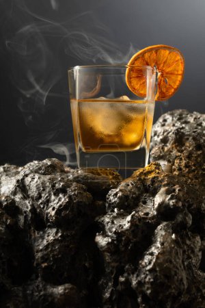 Photo for Smoked old fashioned rum cocktail with ice and dried orange slice on a grey stone. - Royalty Free Image