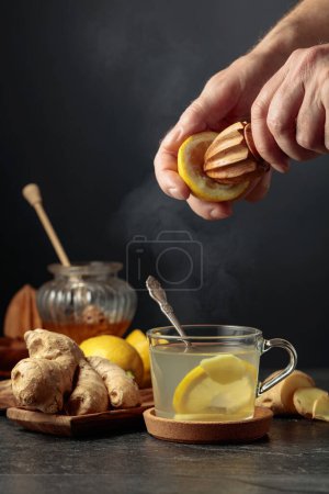 Photo for Ginger tea with lemon and honey. Juice is squeezed out of a lemon with an old wooden juicer. - Royalty Free Image