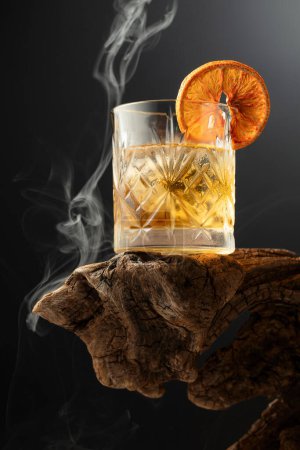 Téléchargez les photos : Cocktail de rhum fumé à l'ancienne avec glace et tranche d'orange séchée sur un vieux chicots en bois. Espace de copie. - en image libre de droit