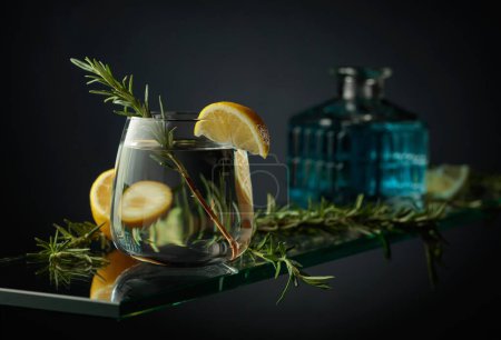 Foto de Refrescante bebida fría con limón y romero. Cóctel de Gin tonic en una mesa de cristal. - Imagen libre de derechos