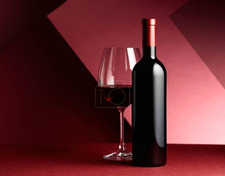 Photo for Bottle and glass of red wine on a red paper background. - Royalty Free Image