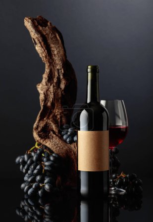 Photo for Bottle of red wine with old empty label. In the background old weathered snag and blue grapes. - Royalty Free Image