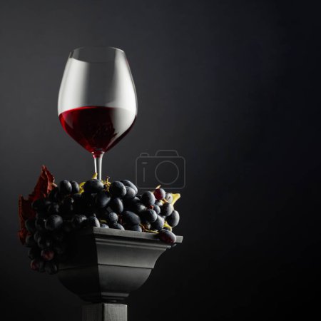Téléchargez les photos : Raisins bleus et un verre de vin rouge sur fond noir. Vue latérale et inférieure. Concentration sélective. Espace de copie. - en image libre de droit
