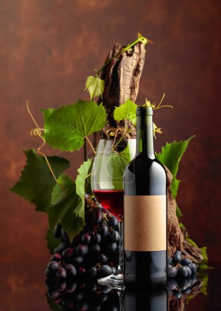 Téléchargez les photos : Verre et bouteille de vin rouge avec raisins bleus et branches de vigne. Sur une vieille étiquette vide. Espace de copie. - en image libre de droit