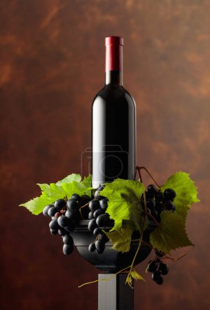 Foto de Botella de rojo en un podio negro. Vino con uvas azules y ramas de vid. Copiar espacio. - Imagen libre de derechos