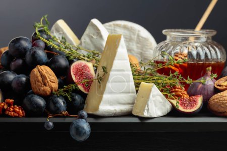 Photo for Camembert cheese with figs, grapes, thyme, walnuts, and honey. Soft cheese with fruits on a black background. - Royalty Free Image